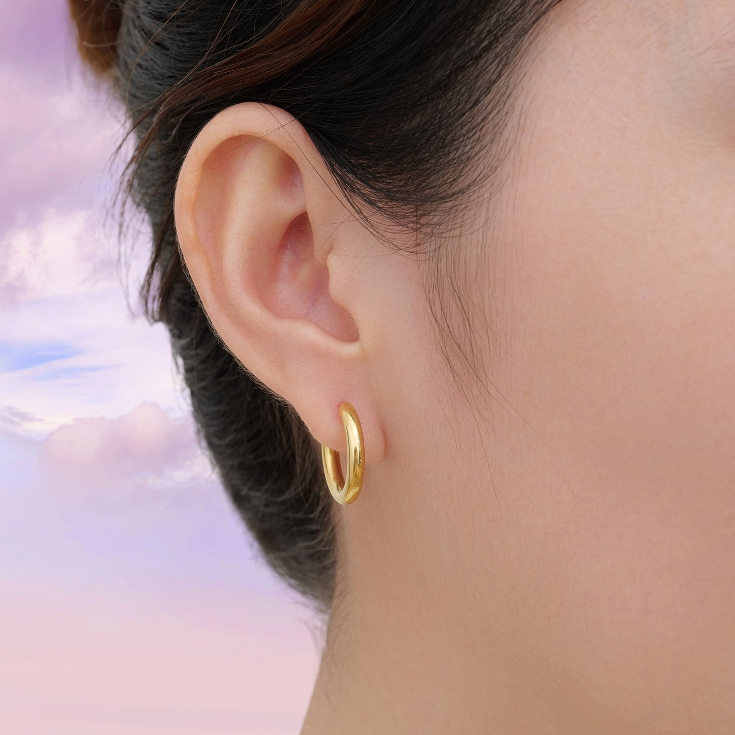 Gold titanium hoop earring worn by a woman with a sky background