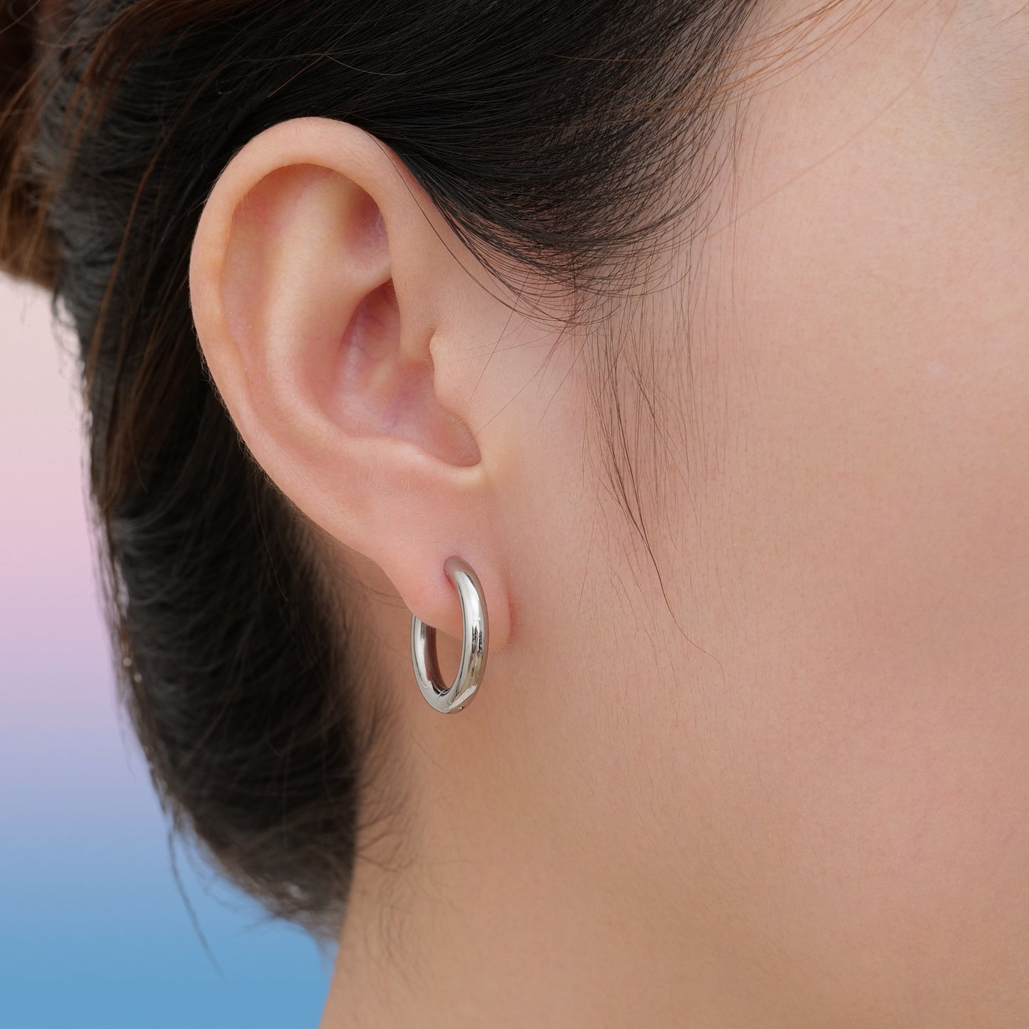 Close-up of an ear wearing a silver titanium hoop earring with a sky background