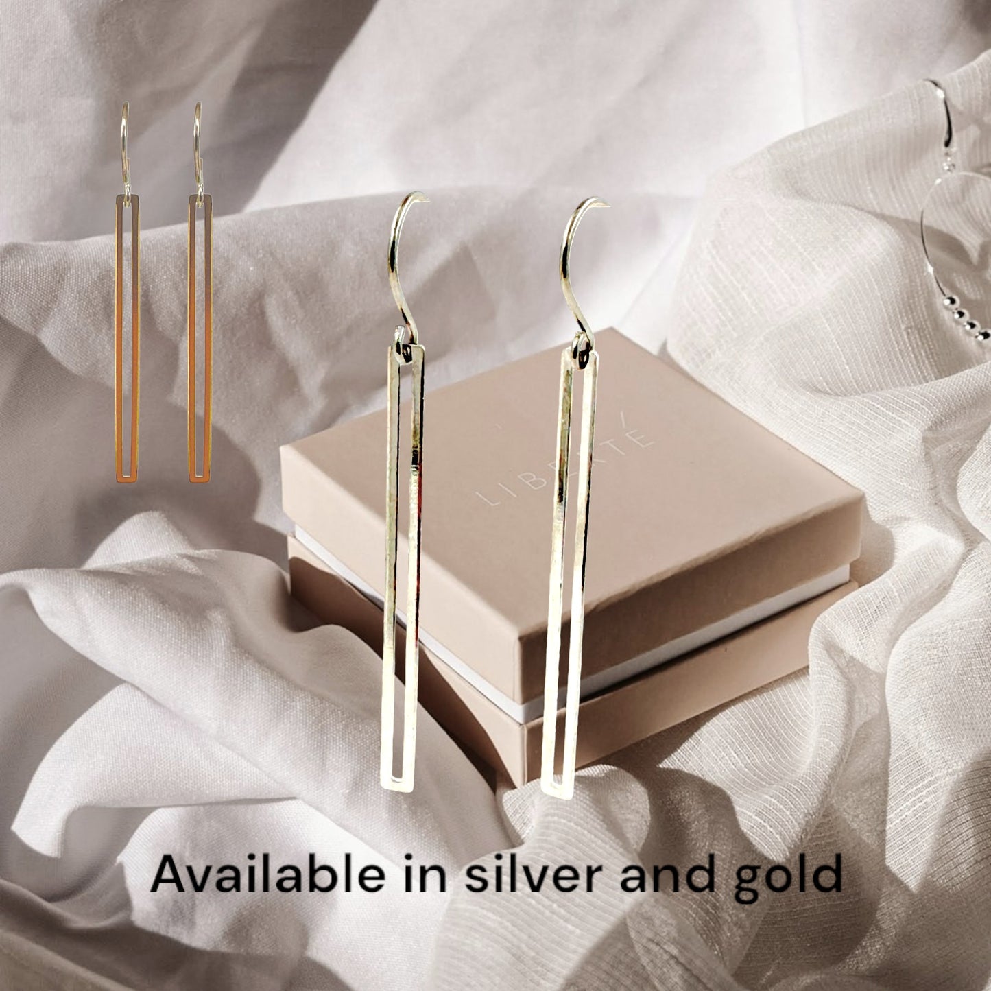 Gold narrow rectangular loop earring with a titanium hook on a white fabric background