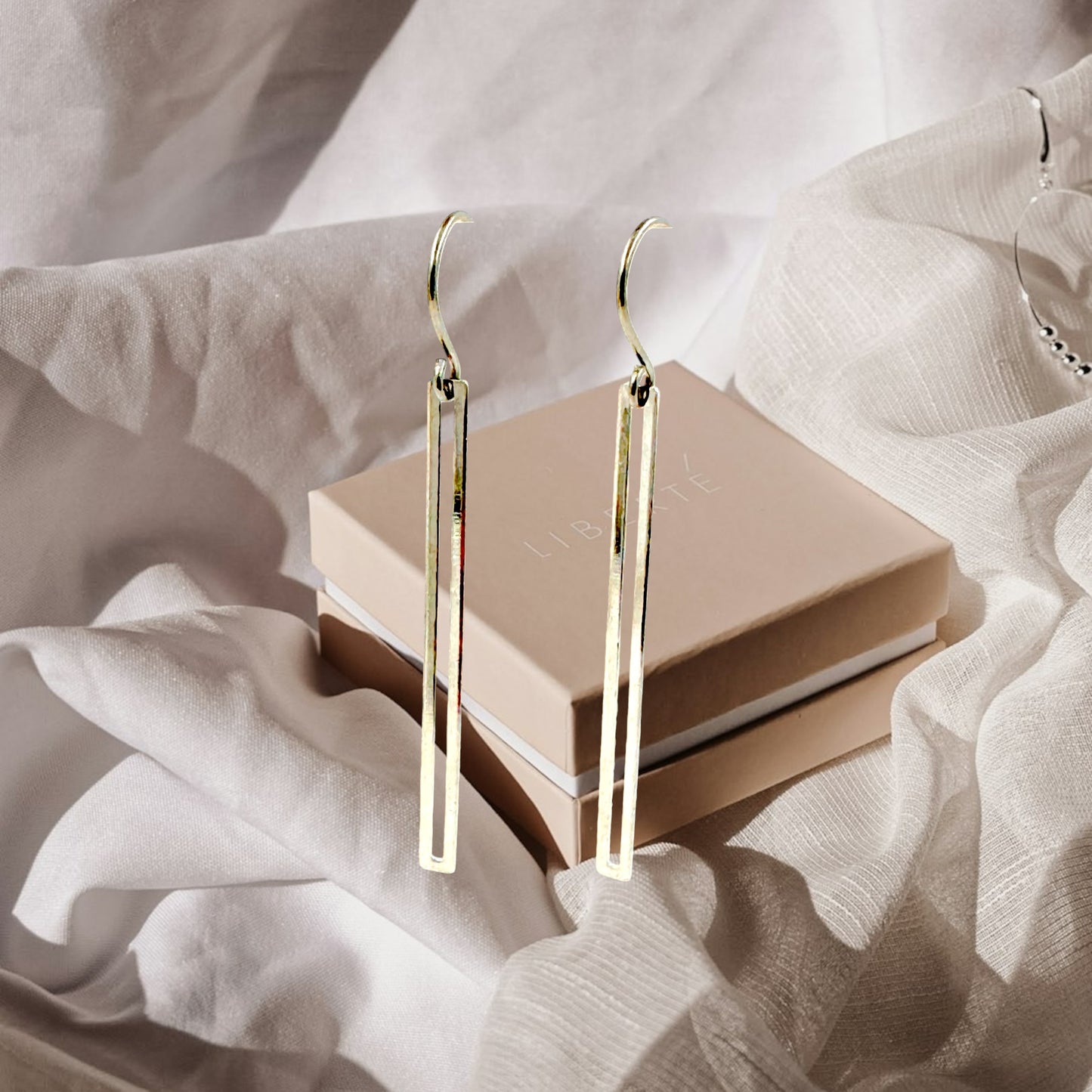 Silver narrow rectangular loop earring with a titanium hook on a white fabric background