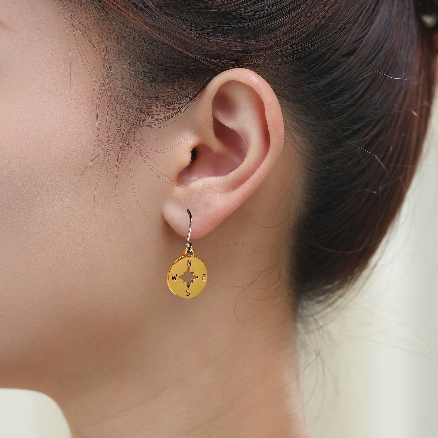 Compass earring with titanium hooks. Shiny gold on a white young woman.