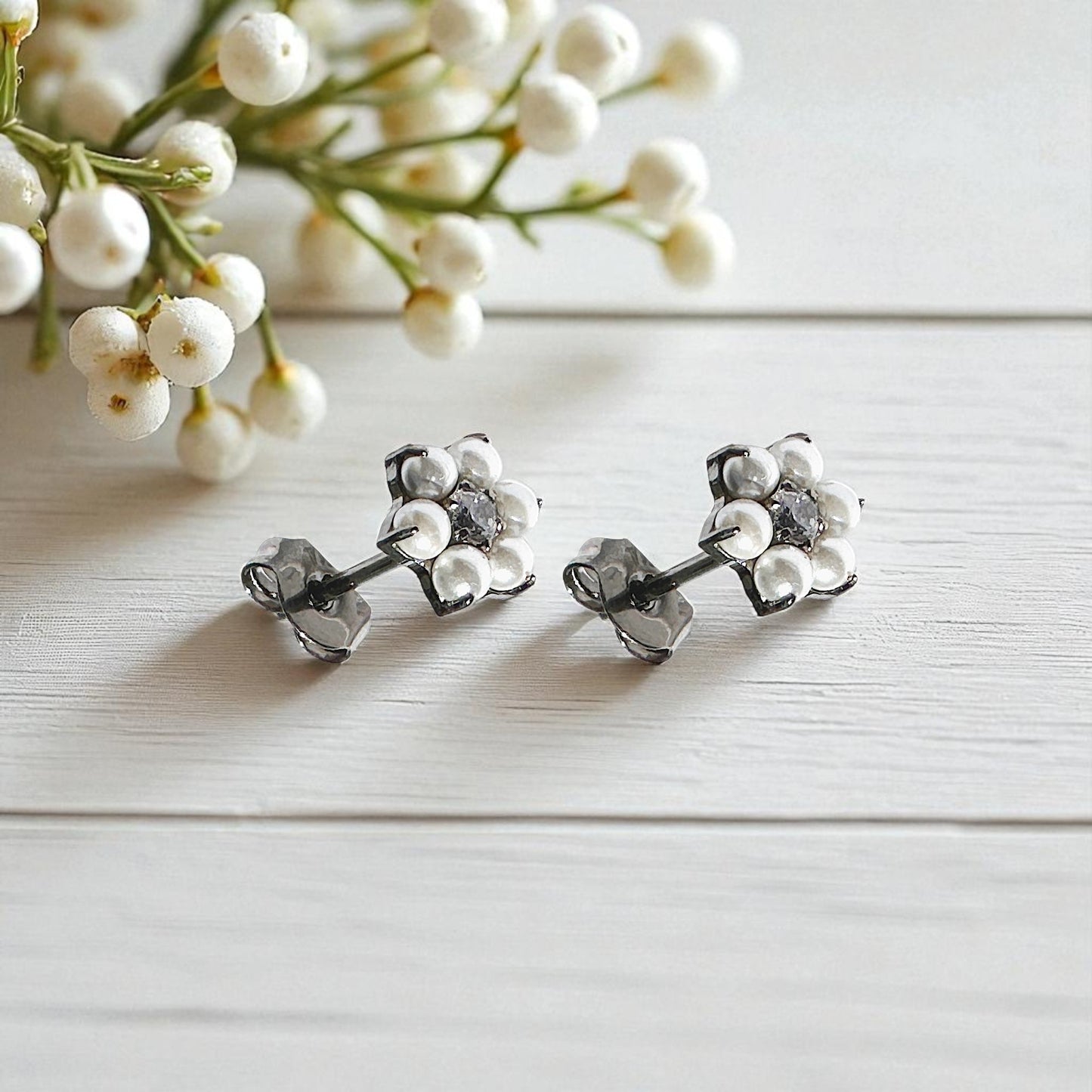 Pair of silver floral titanium earrings on a light wooden surface with white flowers in the background.