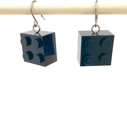 Black titanium lego earrings hanging from a rod against a white background