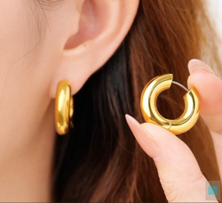 Gold tianium hoop earrings being held near an ear with a blurred background