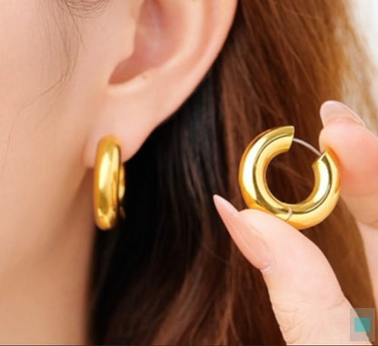 Gold tianium hoop earrings being held near an ear with a blurred background