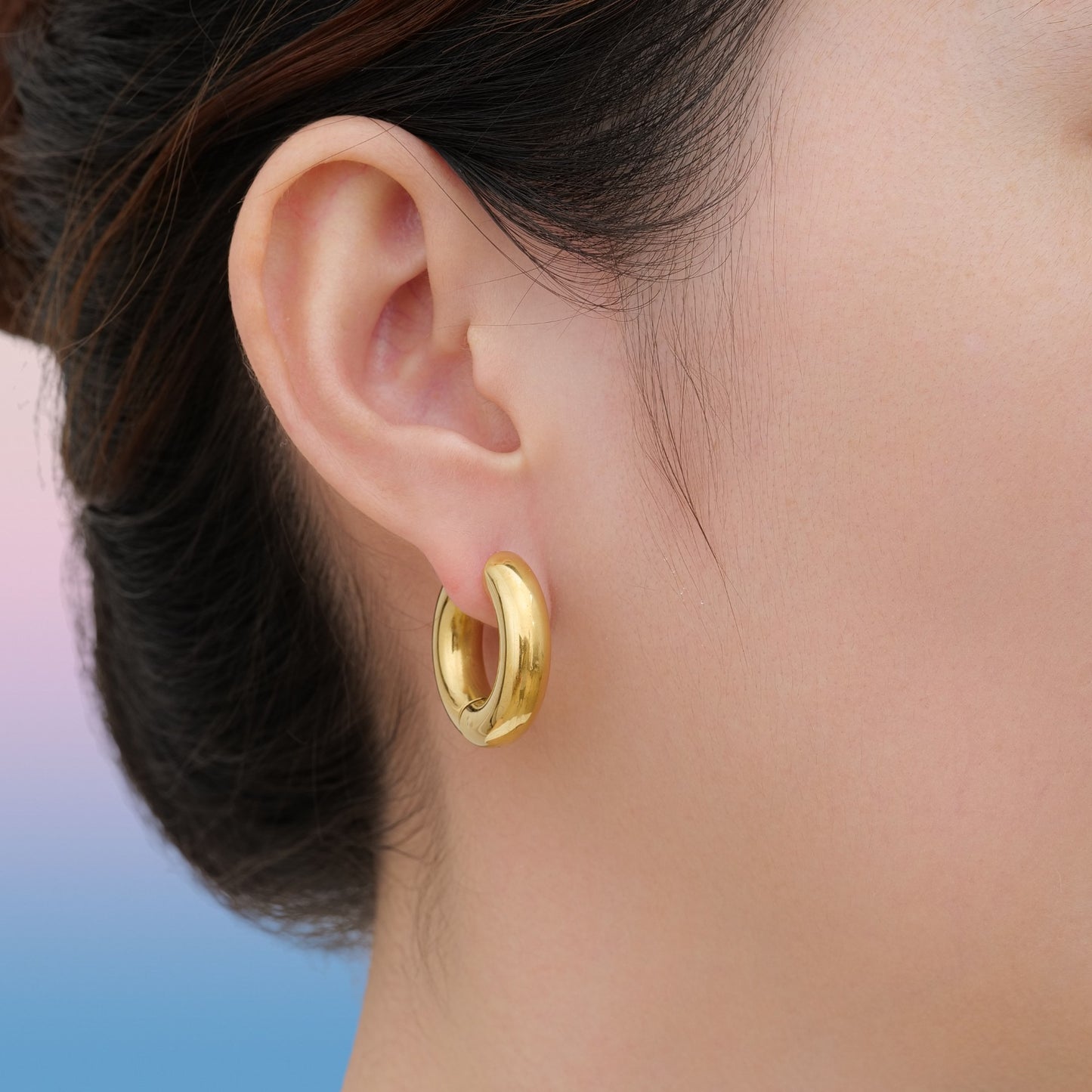 Gold titanium chunky hoop earring worn by a woman with a blurred background