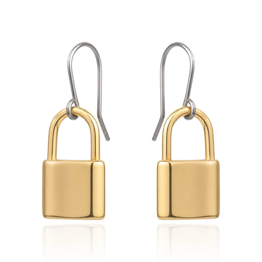 A pair of drop earrings shaped like small padlocks, with polished yellow-gold and titanium hook wires above, shown on a clean white background with a faint reflection below.