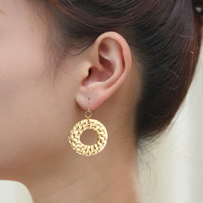 A circular woven straw earring hanging from titanium fishhook wires, on a young woman 