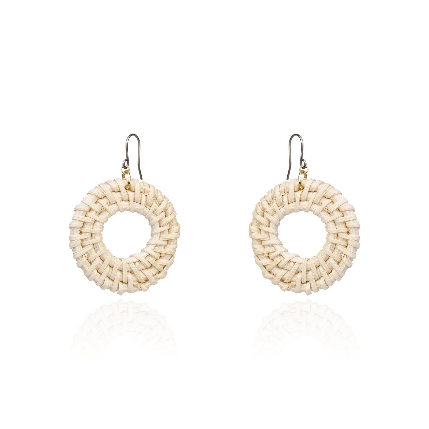 A pair of handmade circular woven earrings made from natural beige raffia or straw, suspended from titanium fishhook wires, shown on a clean white background with a soft reflection below.