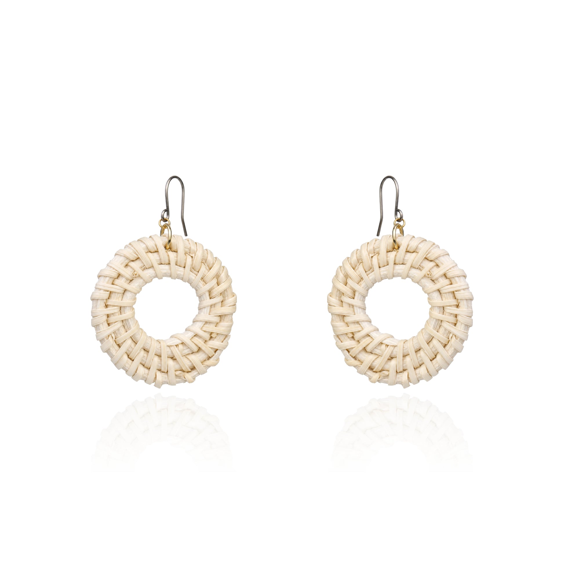 A pair of handmade circular woven earrings made from natural beige raffia or straw, suspended from titanium fishhook wires, shown on a clean white background with a soft reflection below.