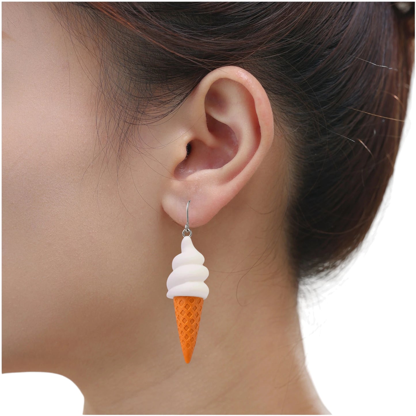 A close-up of a person's ear wearing a dangling ice cream cone earring. The earring has a white soft-serve top and an orange waffle-cone bottom on a titanium hook.