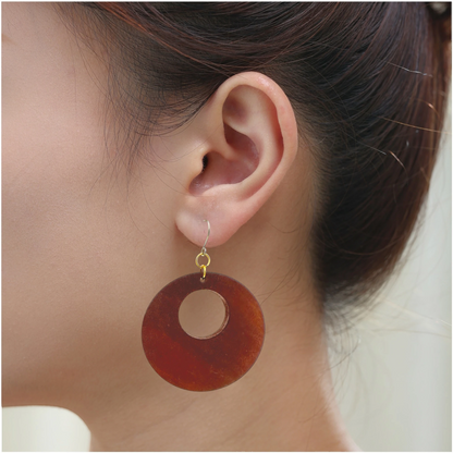 A close-up of a person's ear wearing a single hoop drop earring made of wood brown material with a small titanium hook.
