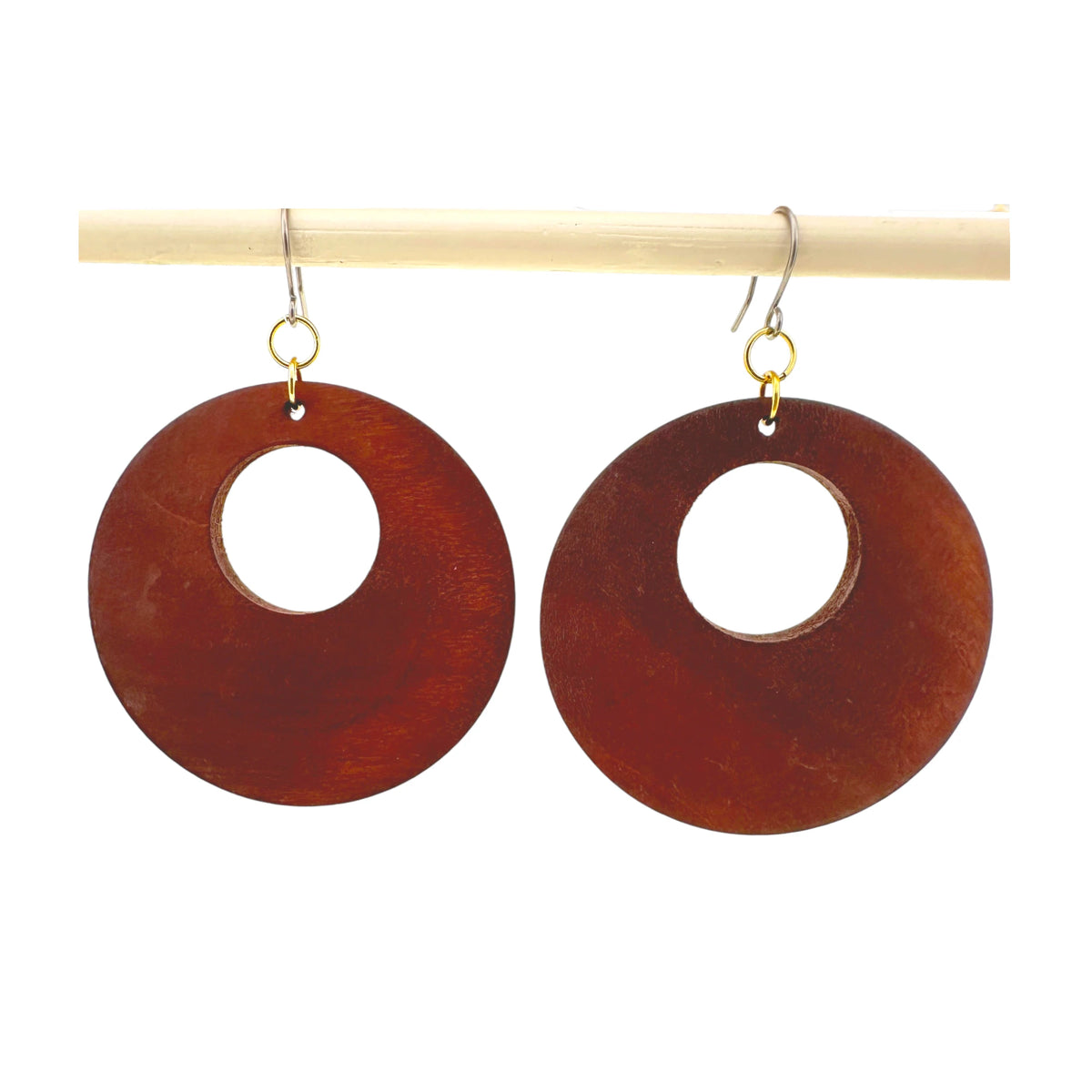 A pair of titanium wooden dangle earrings with a cutout center, hanging from titanium fishhook wires on a light wooden display rod against a white background.