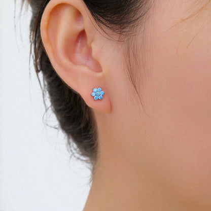 Close-up of an ear wearing a titanium threadless slat back floral aqua blue stud earring with a blurred background