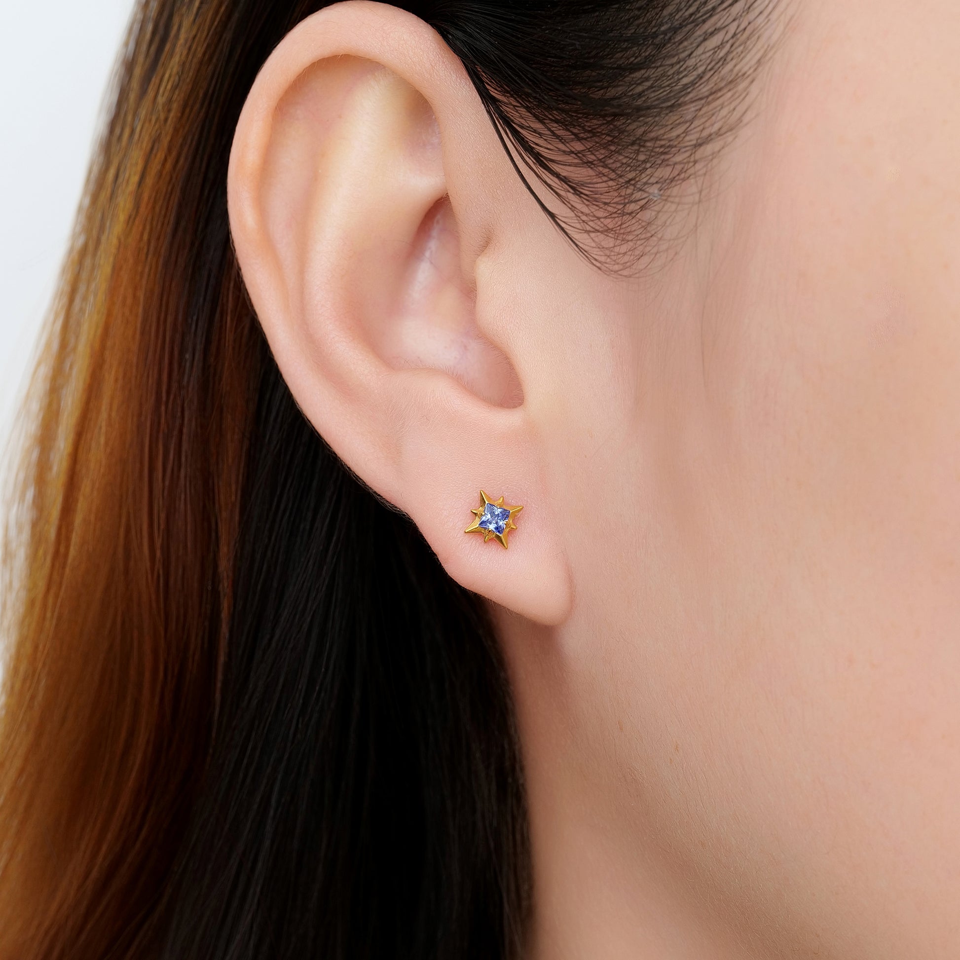 Close-up of an ear wearing a titanium blue gem and gold titanium flat back threadless earring with a blurred background