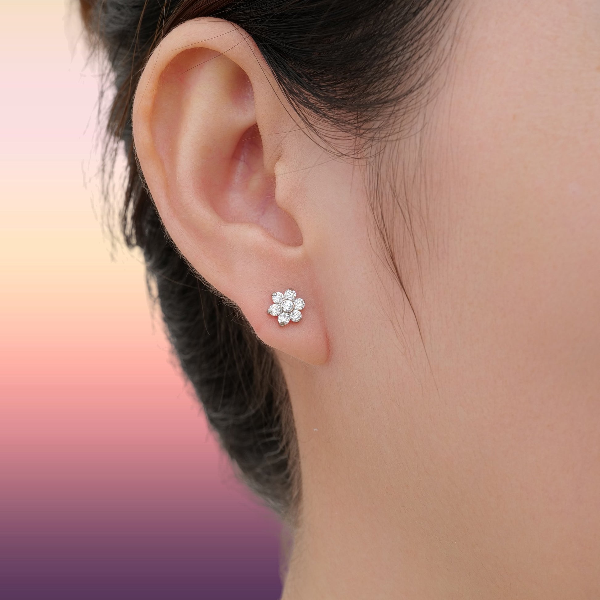 Close-up of an ear wearing a titanium floral stud earring with a blurred background