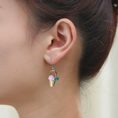 Gardener’s Charm earrings in gold with pink flower and a titanium hook on a white young woman