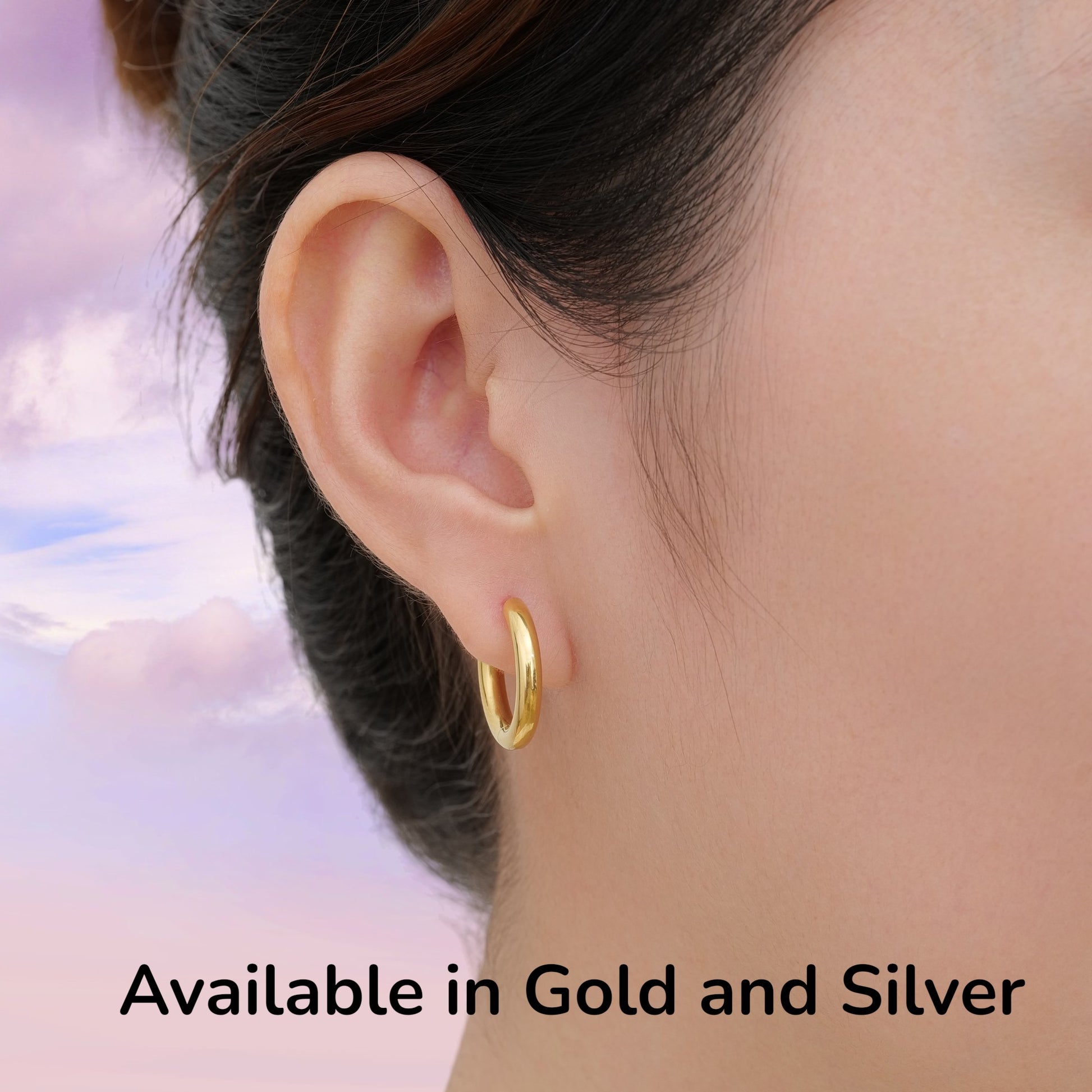 Gold titanium hoop earring worn by a woman with a sky background available in gold or silver