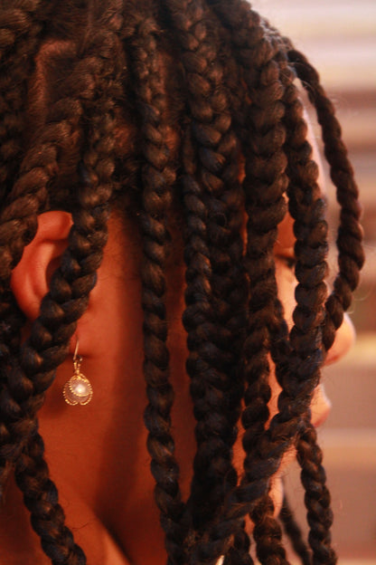 Gold caged pearl earring and a titanium hook on a black young woman.