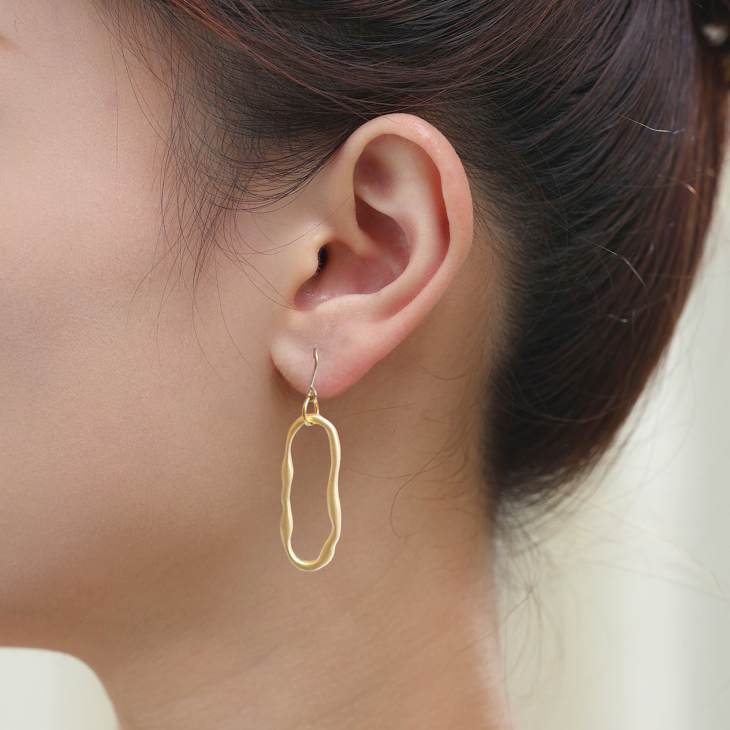 Gold oblong loop minimal earrings with a titanium hook on a white young woman. larger size