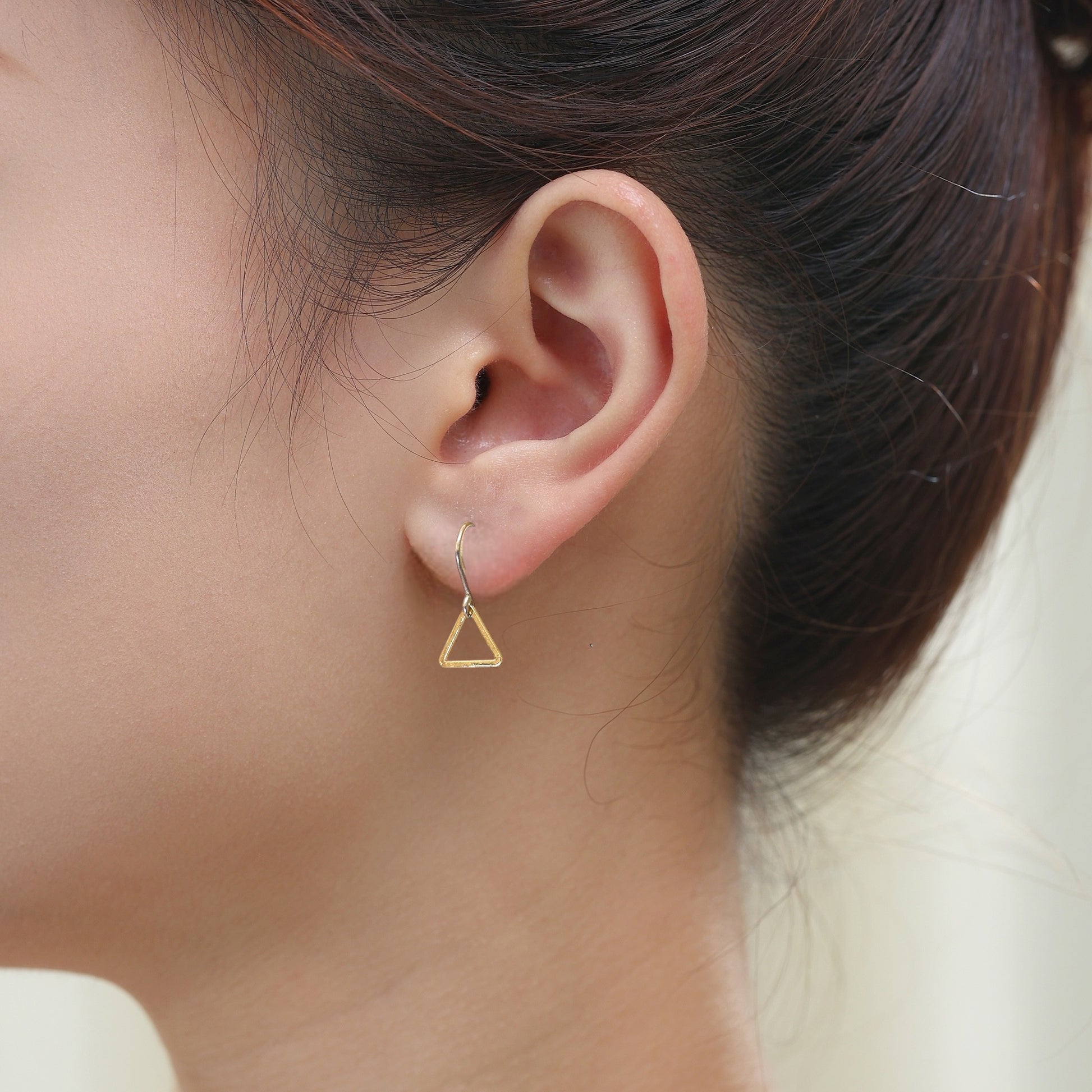 Minimal gold triangle drop earring with a titanium hook on a white young woman