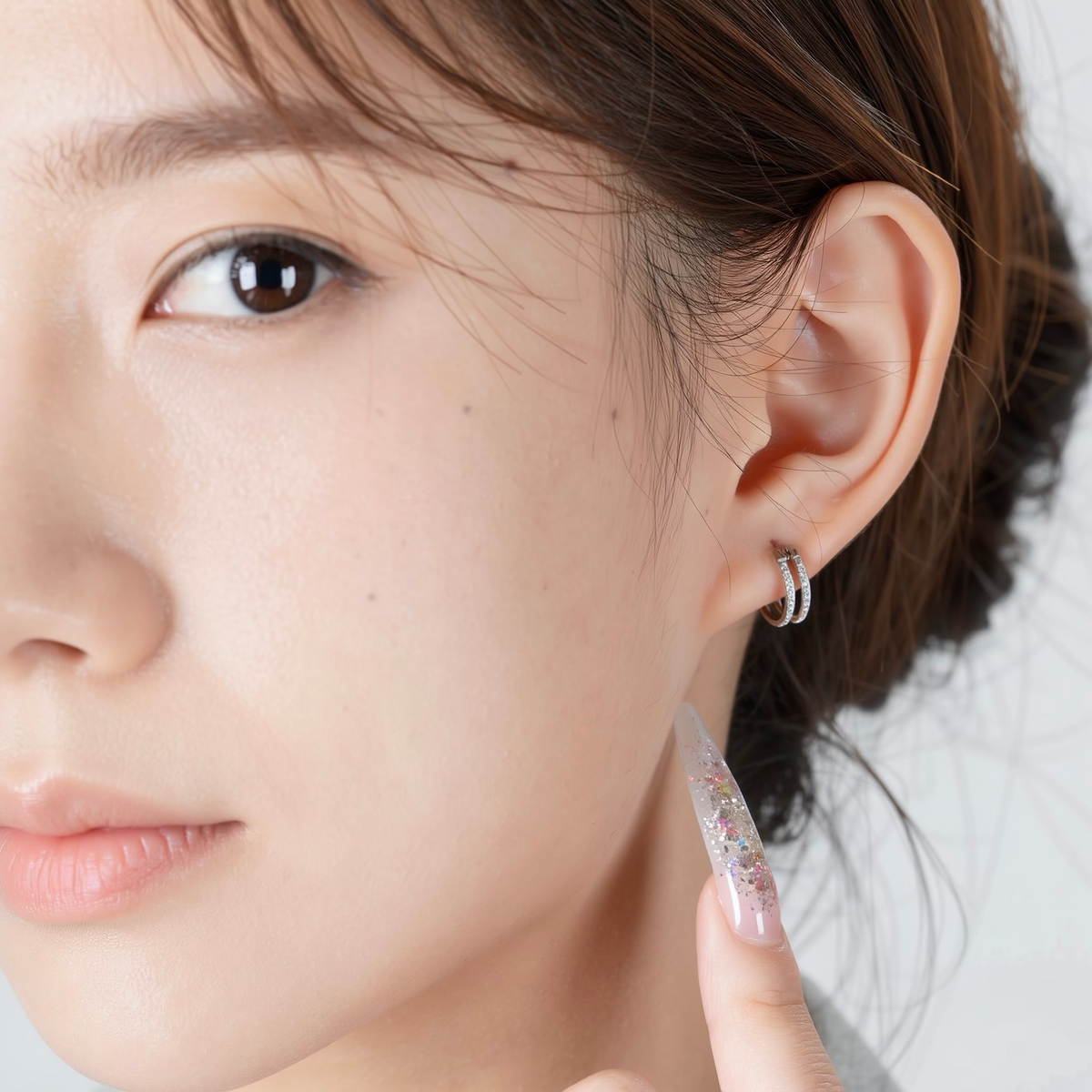 A close-up of a person's ear wearing a titanium small round-shaped hoop earring with diamond gems around both hoops.