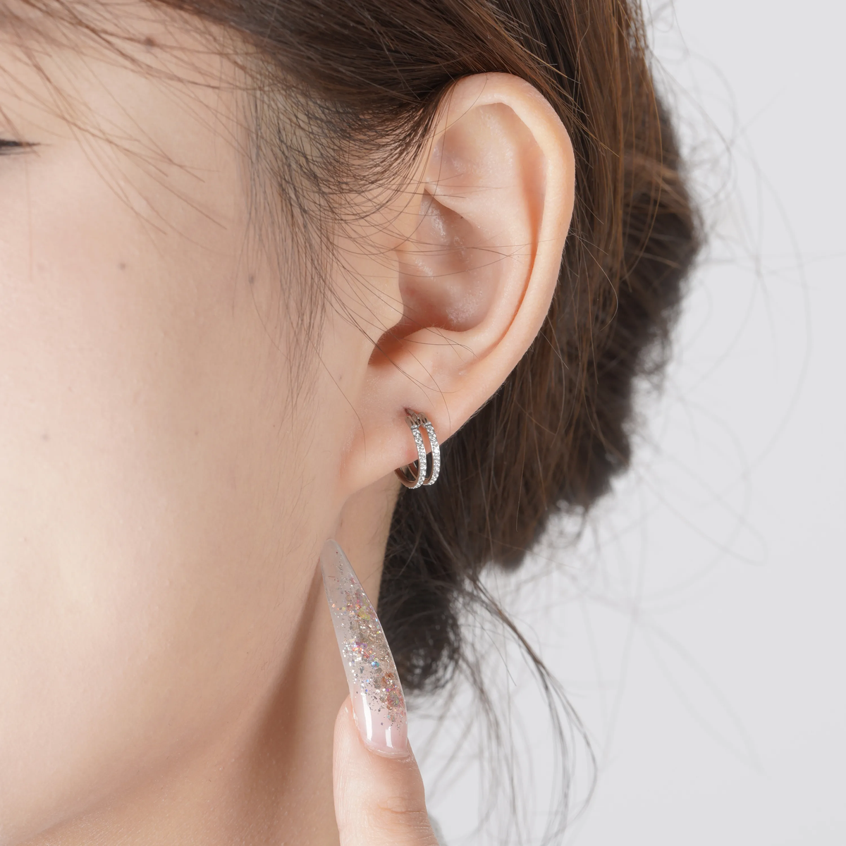 A close-up of a person's ear wearing a titanium small round-shaped hoop earring with diamond gems around both hoops.
