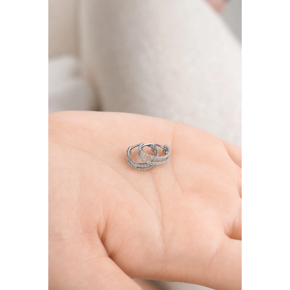 A close-up of a pair of titanium small round-shaped hoop earring with diamond gems around both hoops on a hand