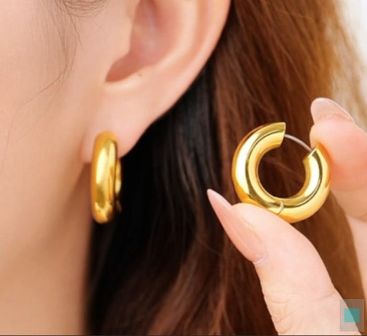Gold tianium hoop earrings being held near an ear with a blurred background