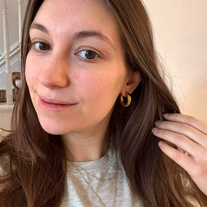 Gold titanium chunky hoop earring worn by a woman house background