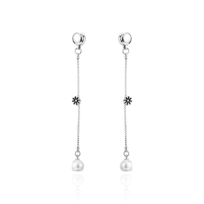 A pair of ti-go titanium interchangeable magnetic dangle earrings with a small flower charm and a white pearl drop, shown on a clean white background with a subtle reflection.