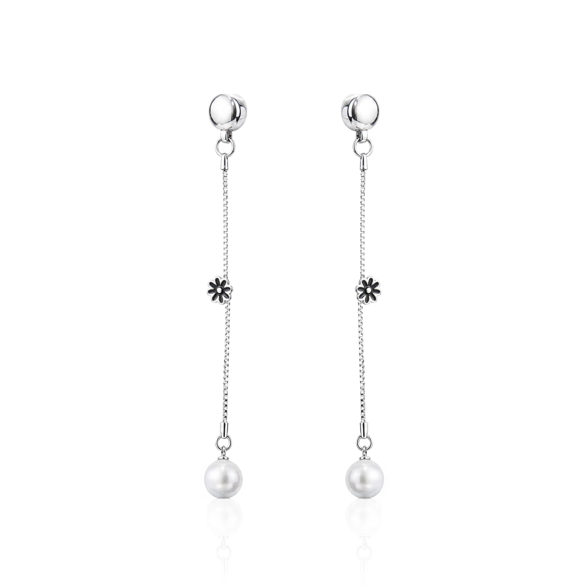 A pair of ti-go titanium interchangeable magnetic dangle earrings with a small flower charm and a white pearl drop, shown on a clean white background with a subtle reflection.