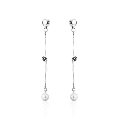 A pair of ti-go titanium interchangeable magnetic dangle earrings with a small flower charm and a white pearl drop, shown on a clean white background with a subtle reflection.