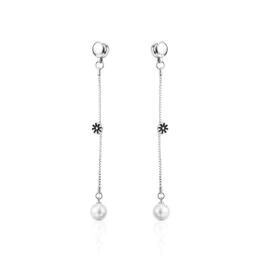 A pair of ti-go titanium interchangeable magnetic dangle earrings with a small flower charm and a white pearl drop, shown on a clean white background with a subtle reflection.