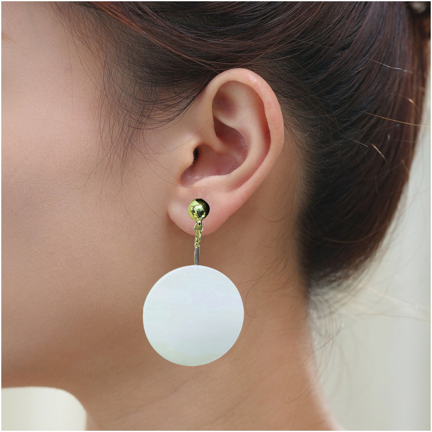 Gold drop earring with a hanging wooden disc. Detachable earrings for a truly hypoallergenic jewellery on a white young woman