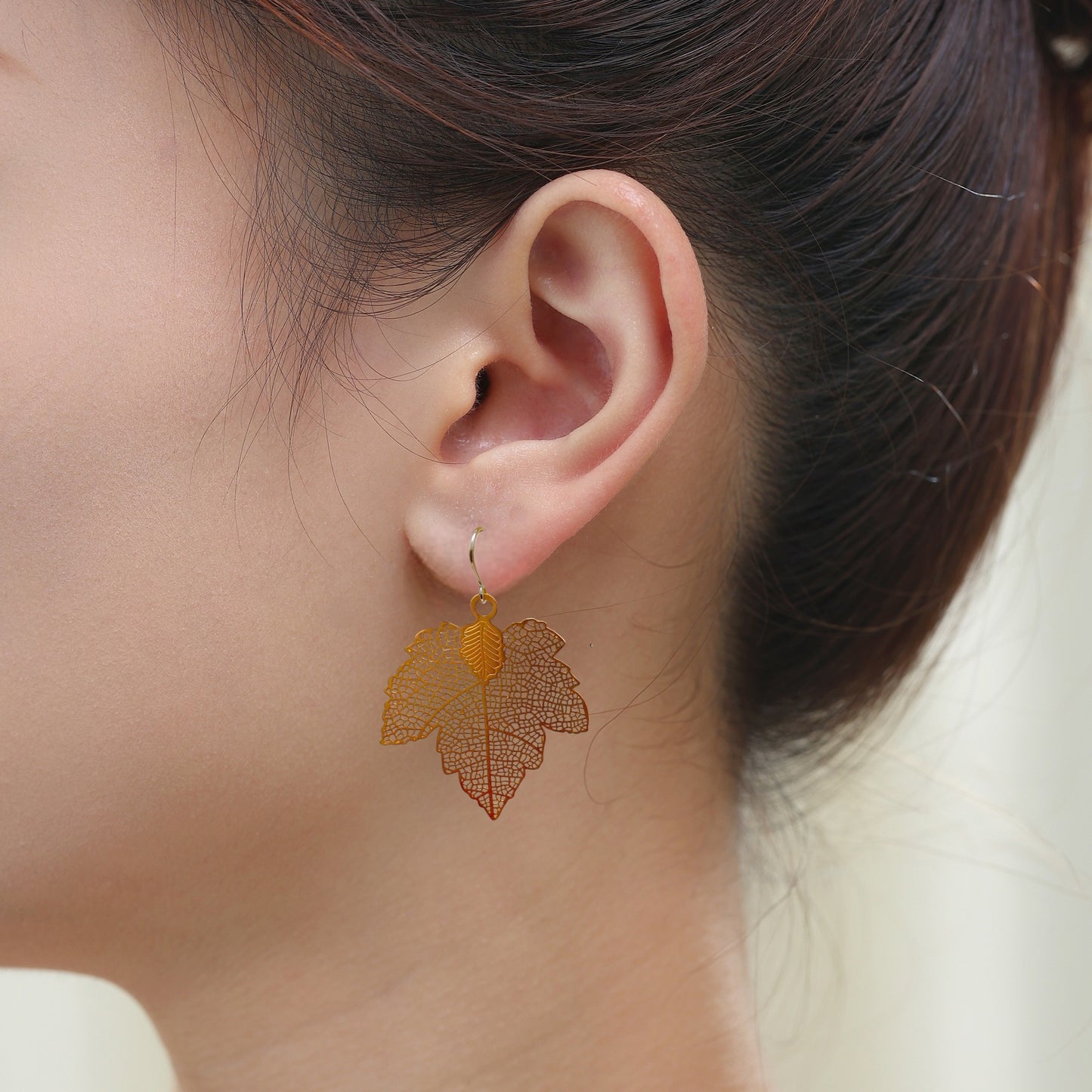 Maple leaf gold leaf earring with a titanium hook on a white young woman