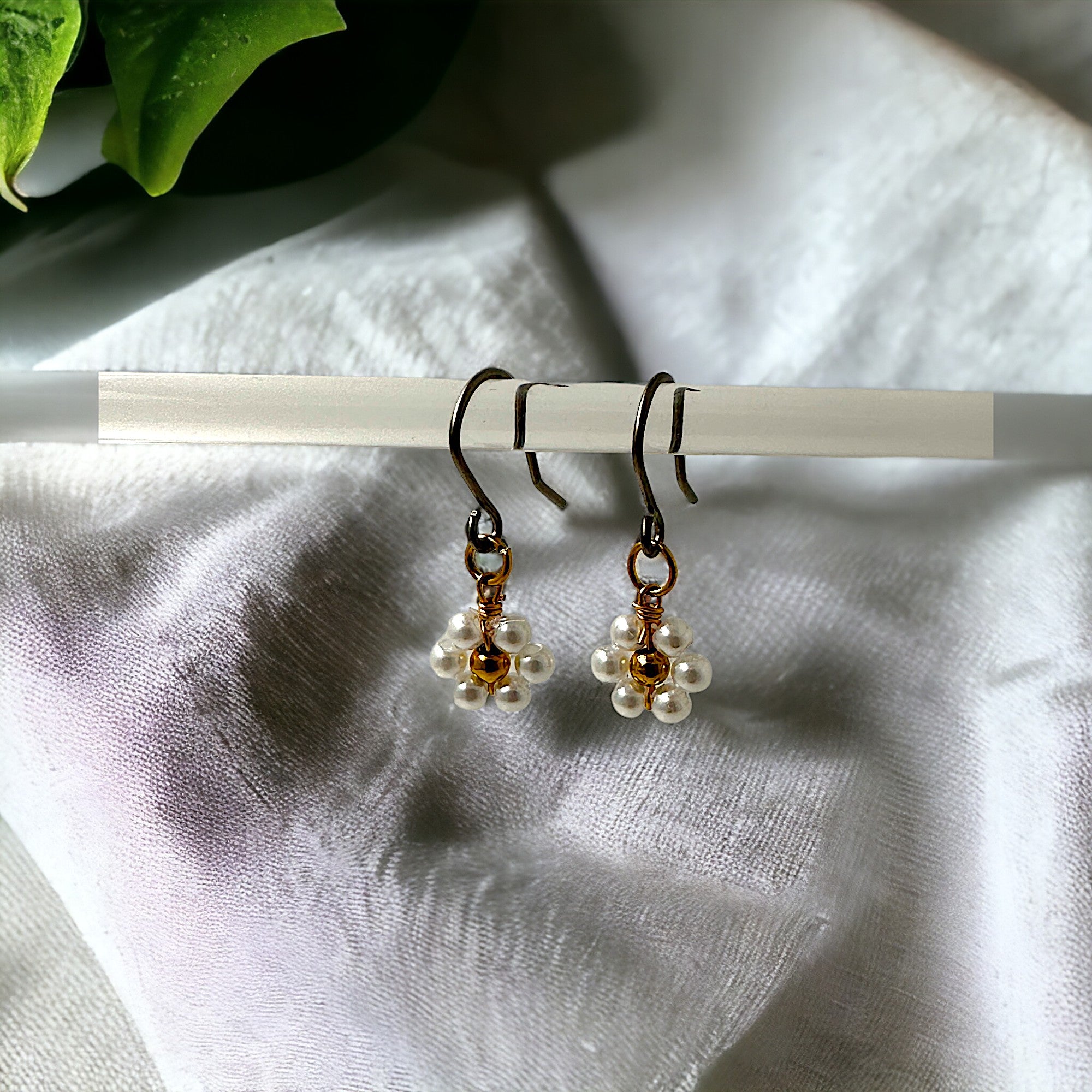 Mini pearl flower cluster earrings with a titanium hook on a white and green background