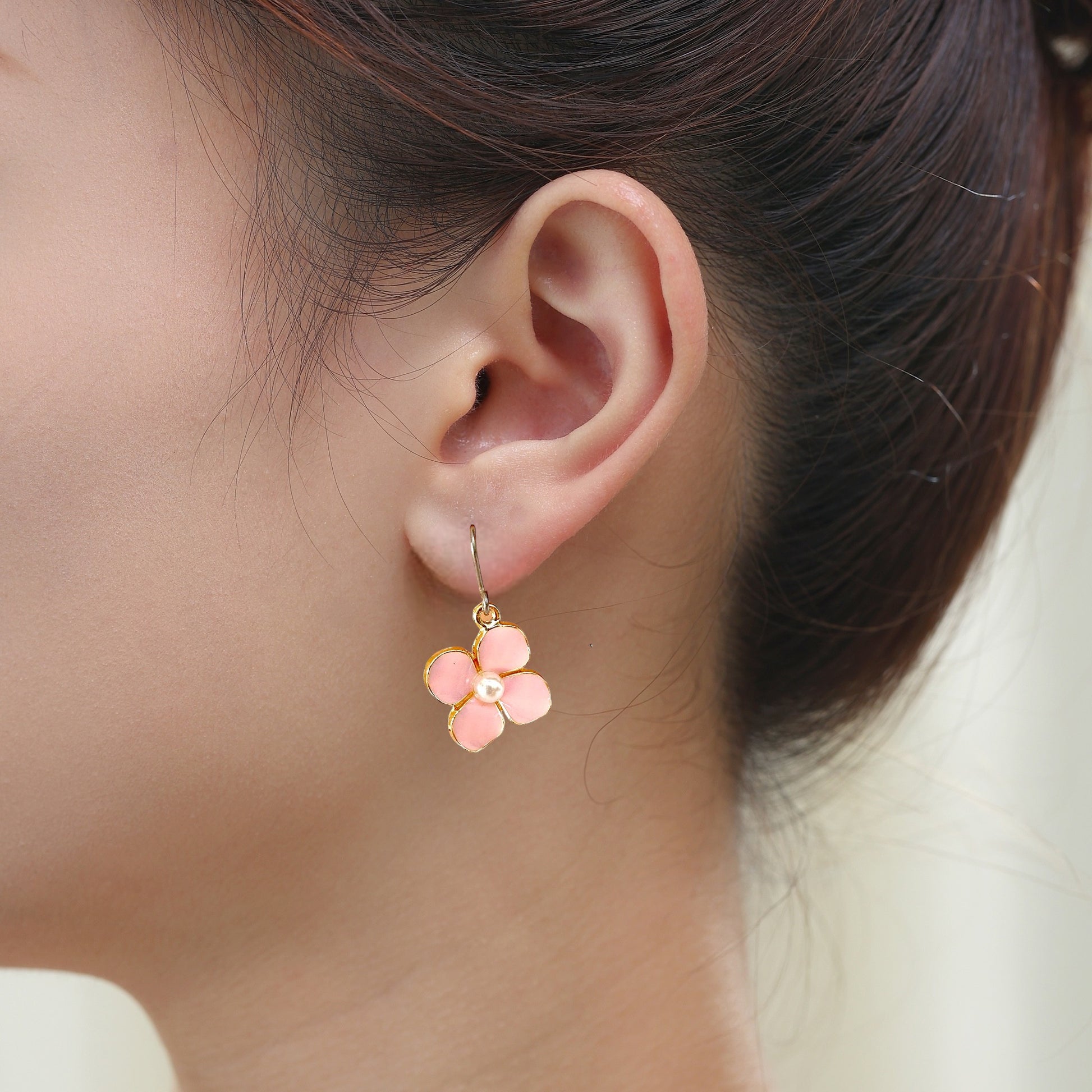 Forget Me Not earrings in pink with a pearl in the center and a titanium hook on a white young woman