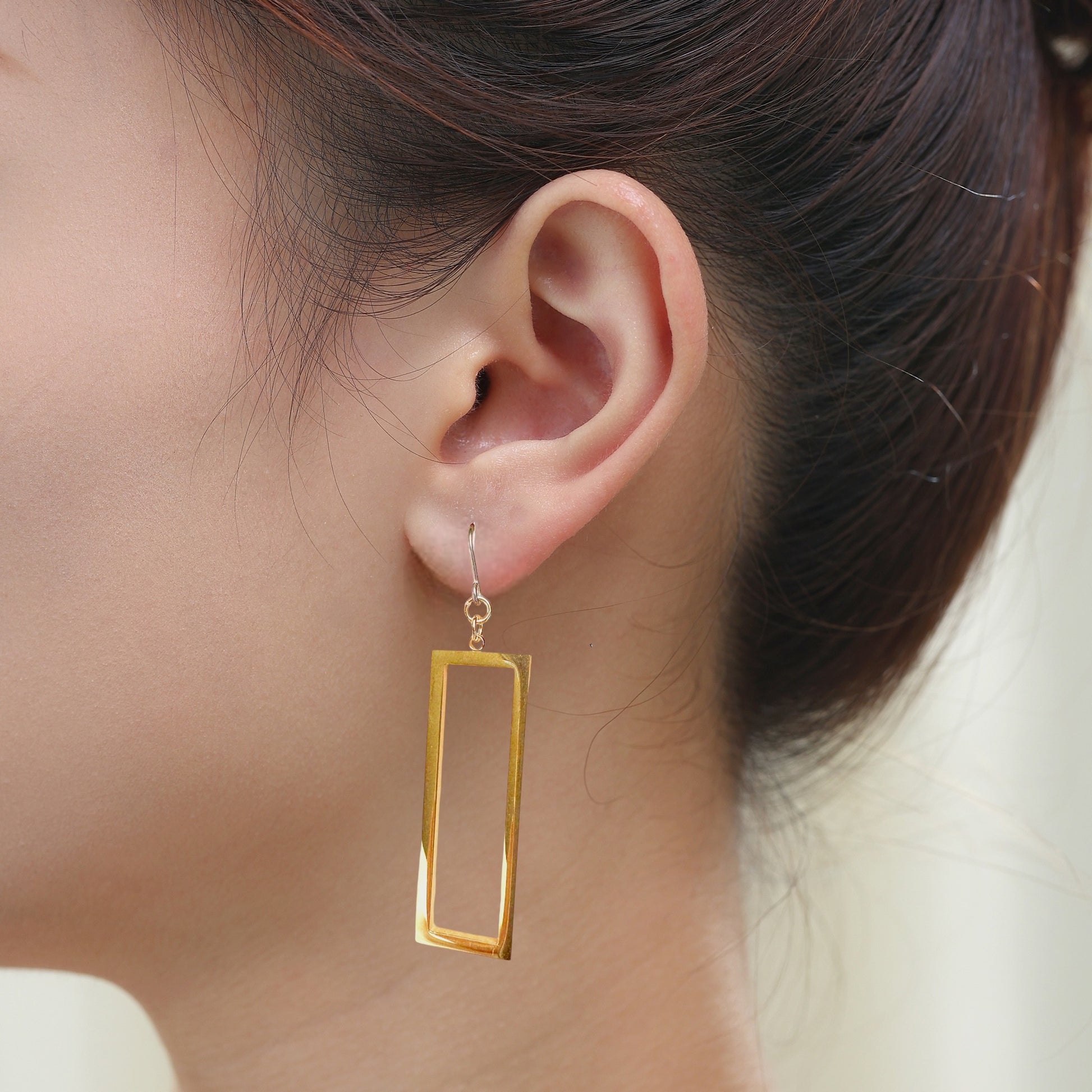 Rectangle mirrored gold earrings with a titanium hook on a white young woman