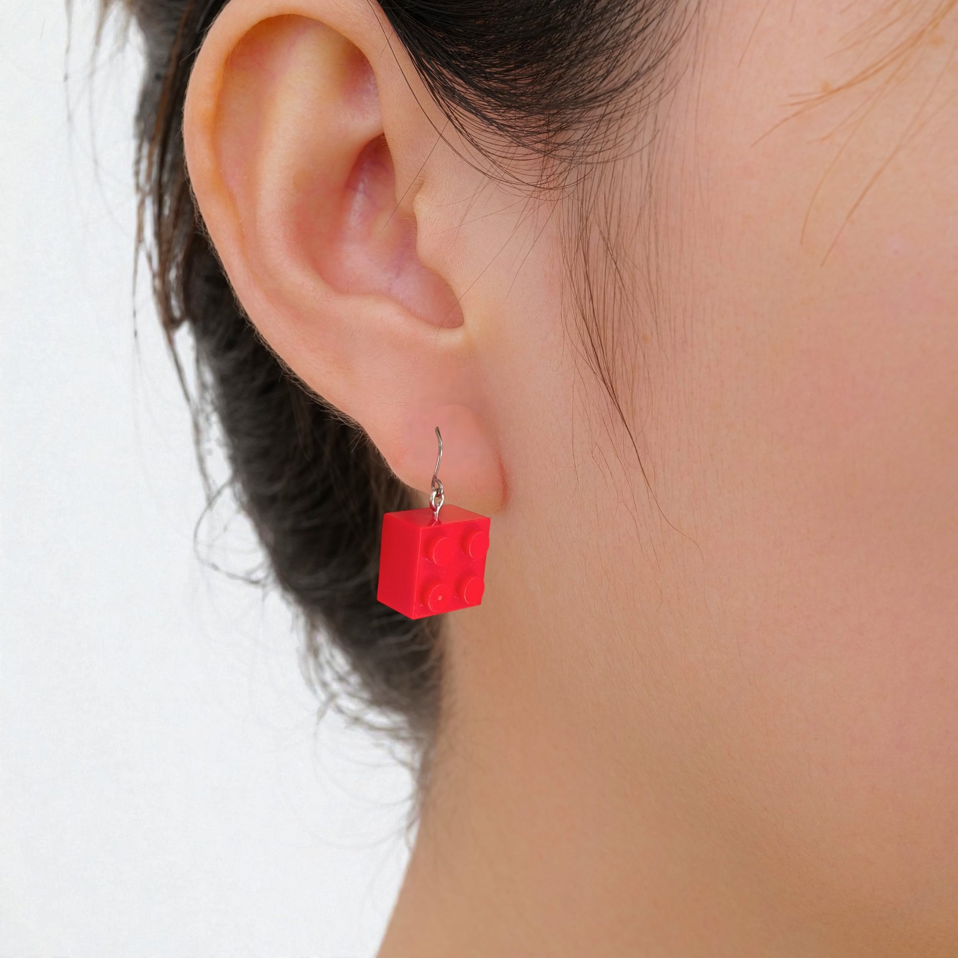 Red titanium lego earrings worn by a person on a white background