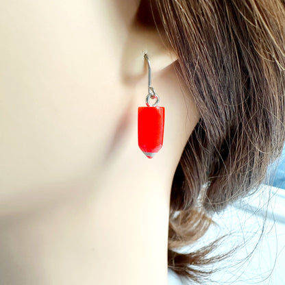 Pencil earrings with a titanium hook on a white young woman. red