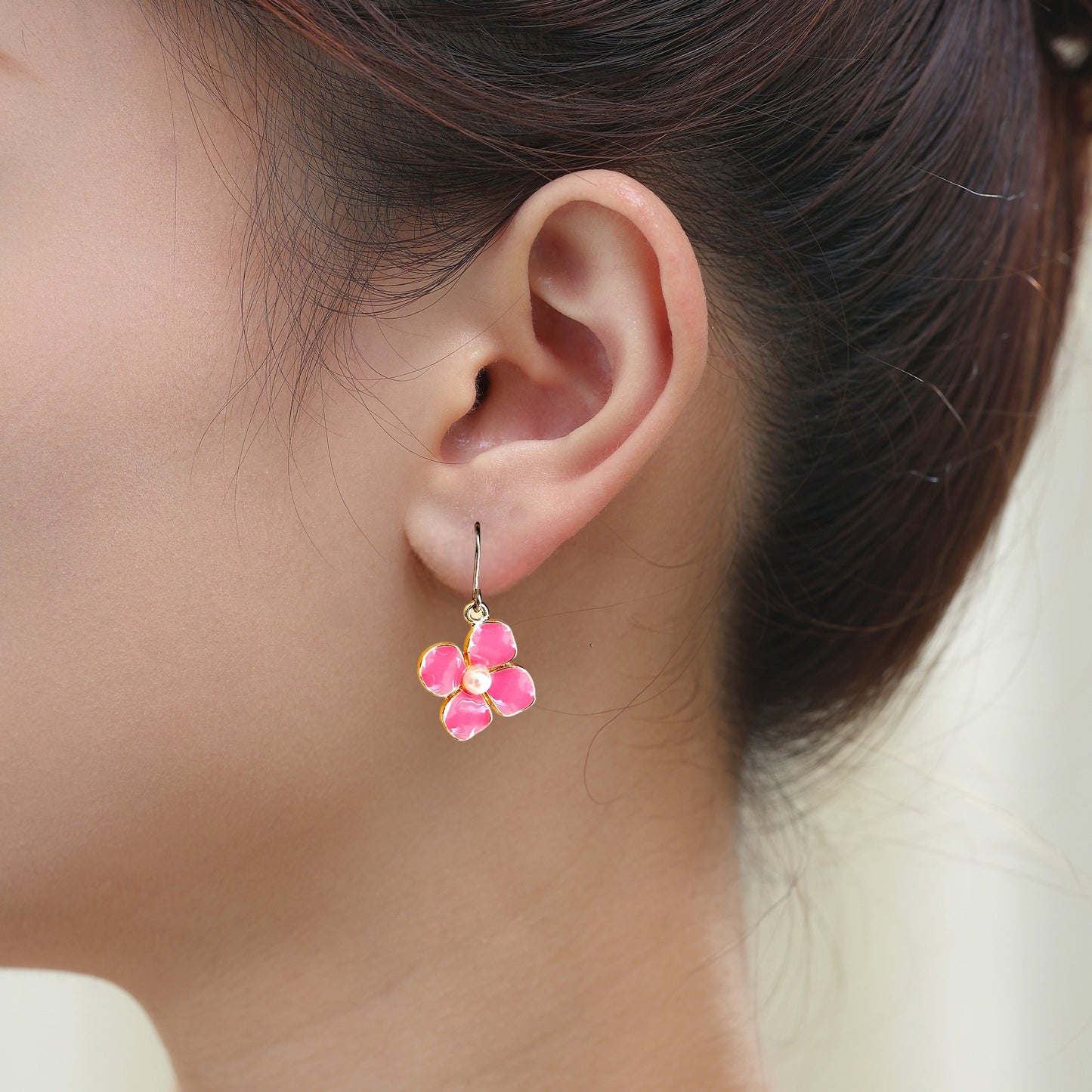 Forget Me Not earrings in rose pink with a pearl in the center and a titanium hook on a white young woman