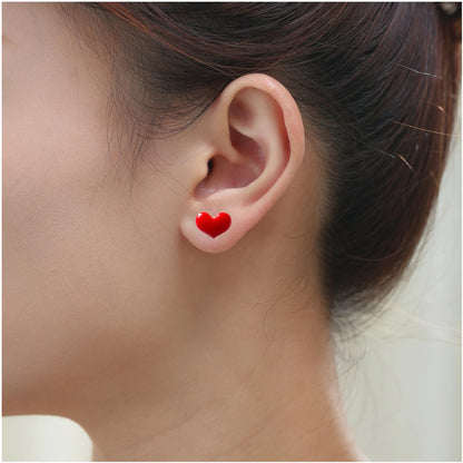 A close-up of a person's ear wearing a titanium small red heart-shaped stud earring.