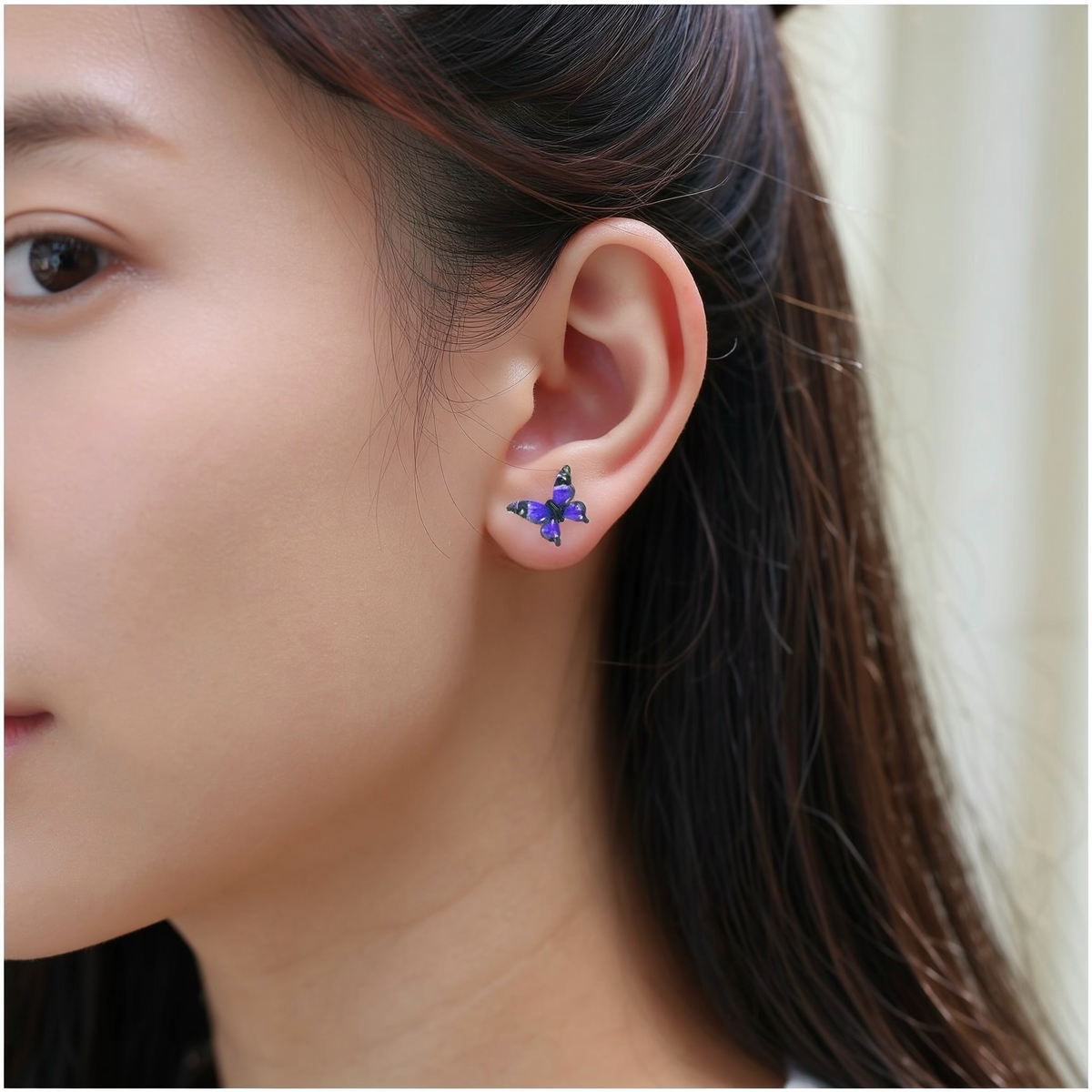 A close-up of a person's ear wearing a small butterfly-shaped titanium stud earring in shades of purple, blue.