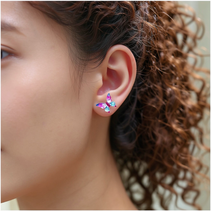 A close-up of a person's ear wearing a small butterfly-shaped titanium stud earring in shades of pink, blue.