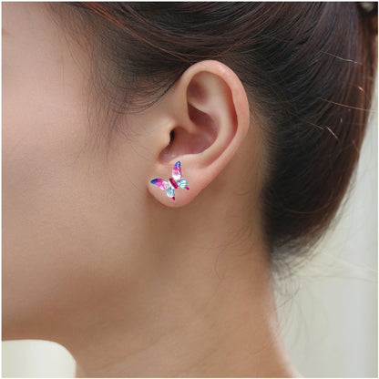 A close-up of a person's ear wearing a small butterfly-shaped titanium stud earring in shades of pink, blue.