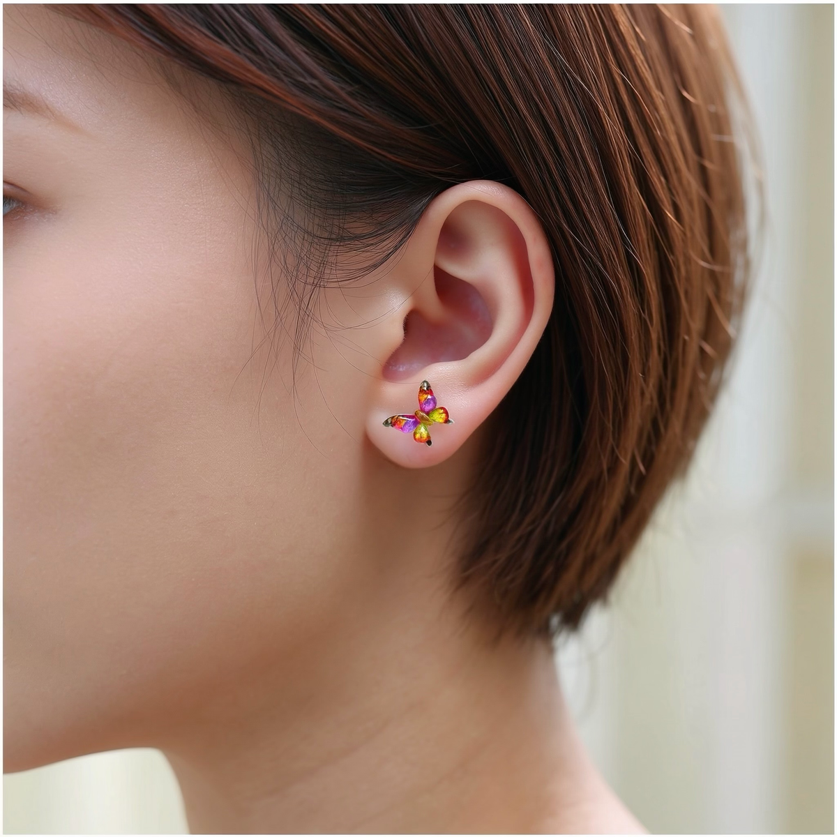 A close-up of a person's ear wearing a small butterfly-shaped titanium stud earring in shades of Yellow, purple.