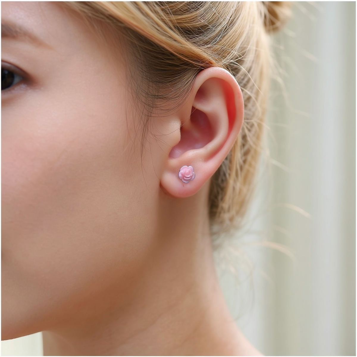 A close-up of a woman wearing a small light pink rose-shaped titanium stud earring.