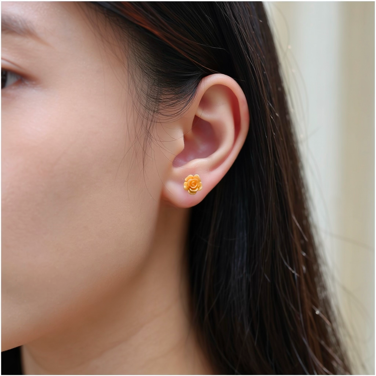 A close-up of a womans ear wearing a small pastel rose-shaped titanium stud earring.