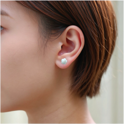A close-up of a person's ear wearing a small white rose-shaped stud earring. 